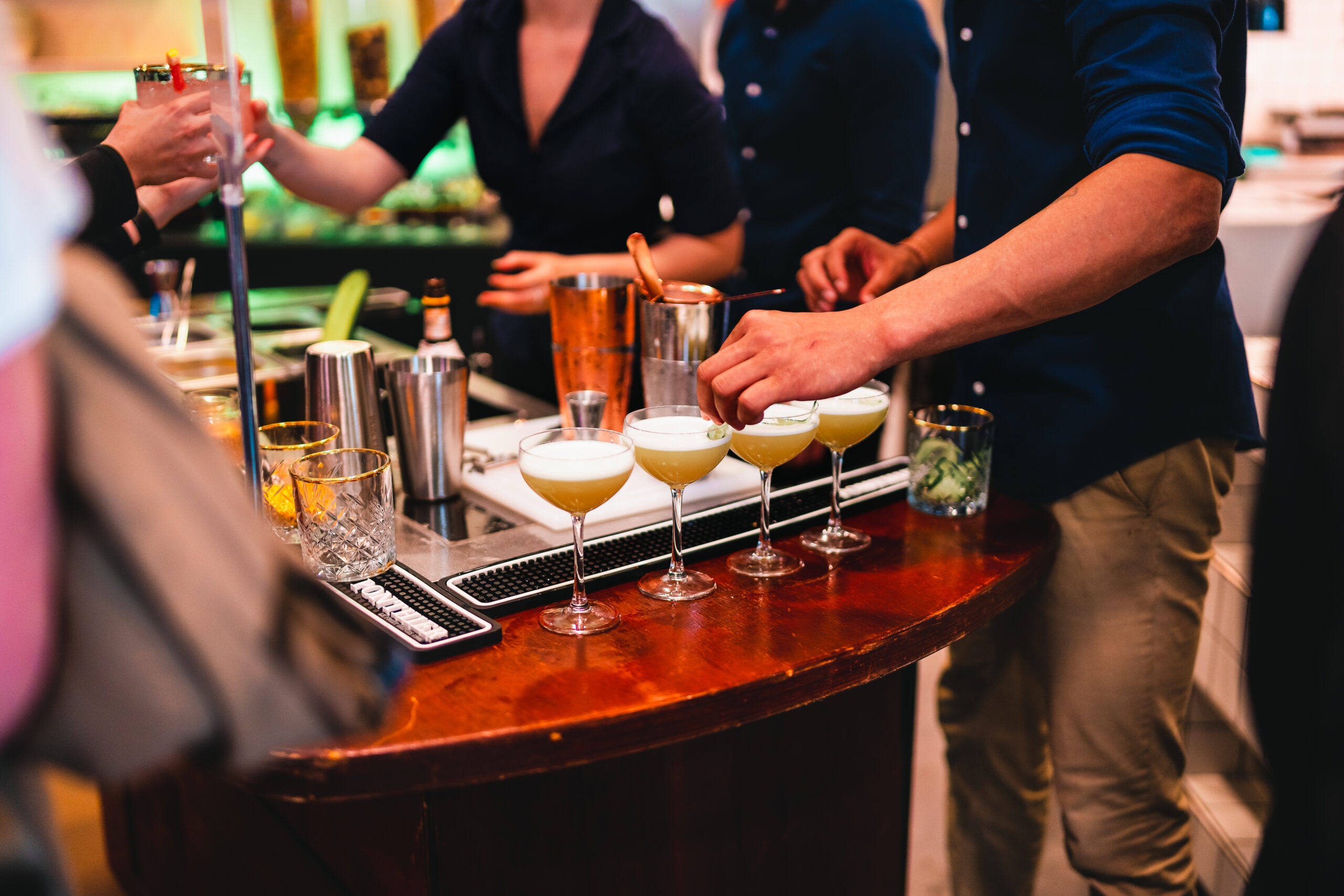 Bartenders bereiden cocktails met zorg en stijl aan een houten bar tijdens een evenement.