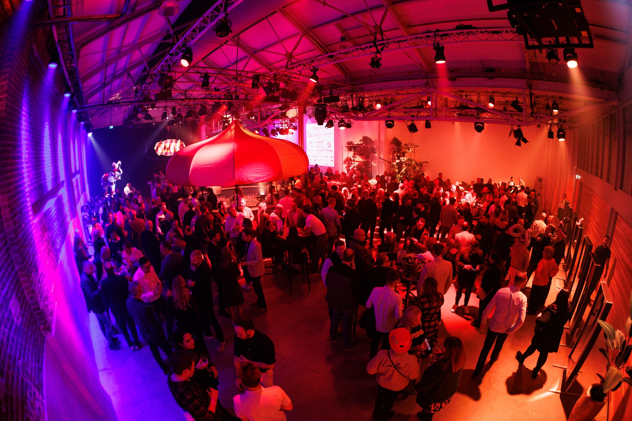 Overzicht van een drukbezochte zaal met kleurrijke verlichting en een centraal circuselement tijdens het ANG netwerkevent.