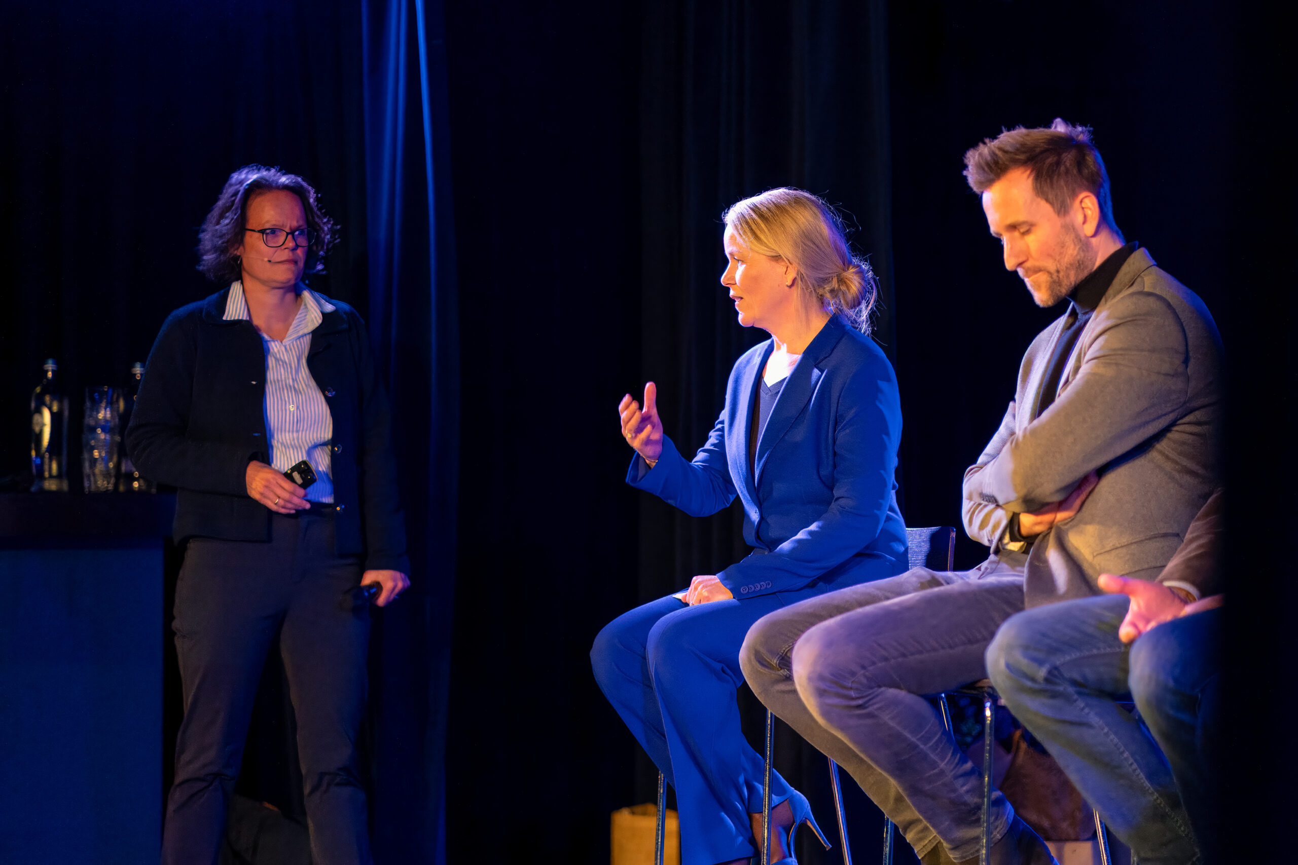 Drie sprekers in gesprek tijdens een paneldiscussie op het podium.