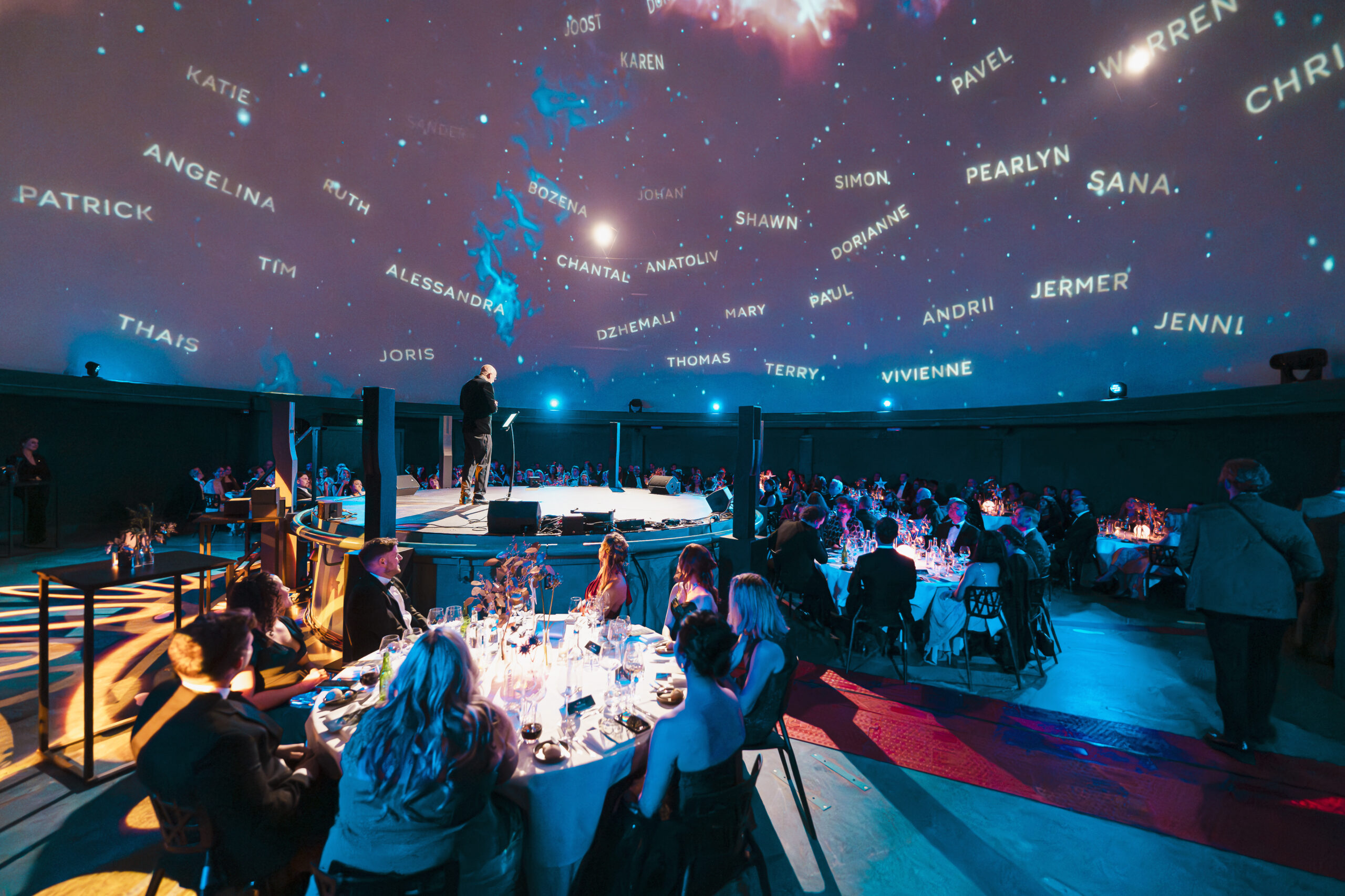 Een dineropstelling in een grote zaal met een sterrenprojectie op het plafond.