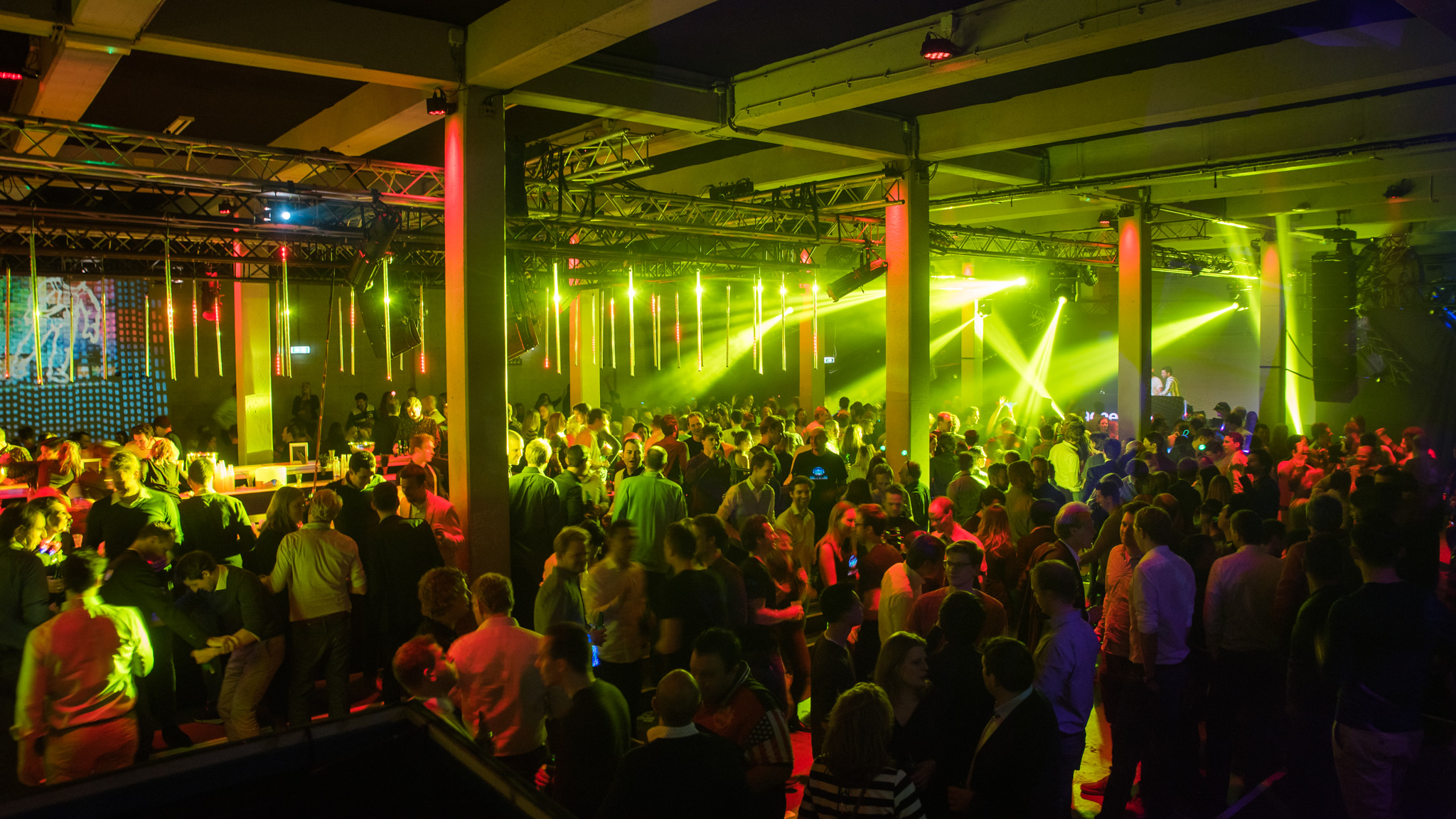 Een volle zaal met mensen die dansen op een evenement met kleurrijke lichten.